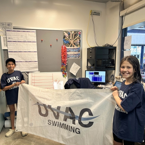 UVAC Swimmers Diya Naren and Saya Brown holding the UVAC swim banner at the 2025 10 And Under Championship Meet